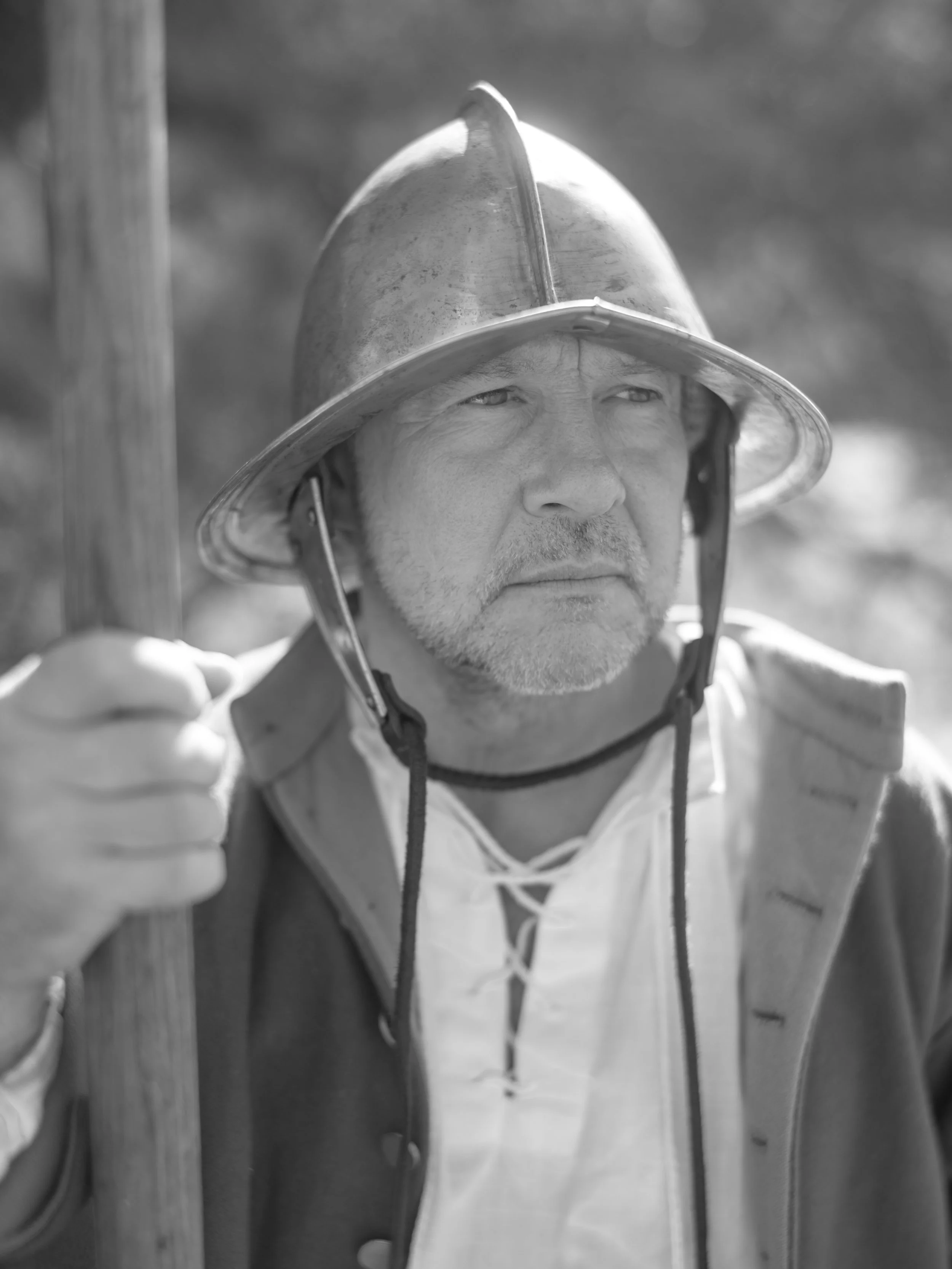 A man dressed as a firefighter wearing a helmet and holding a wooden tool, looking serious.