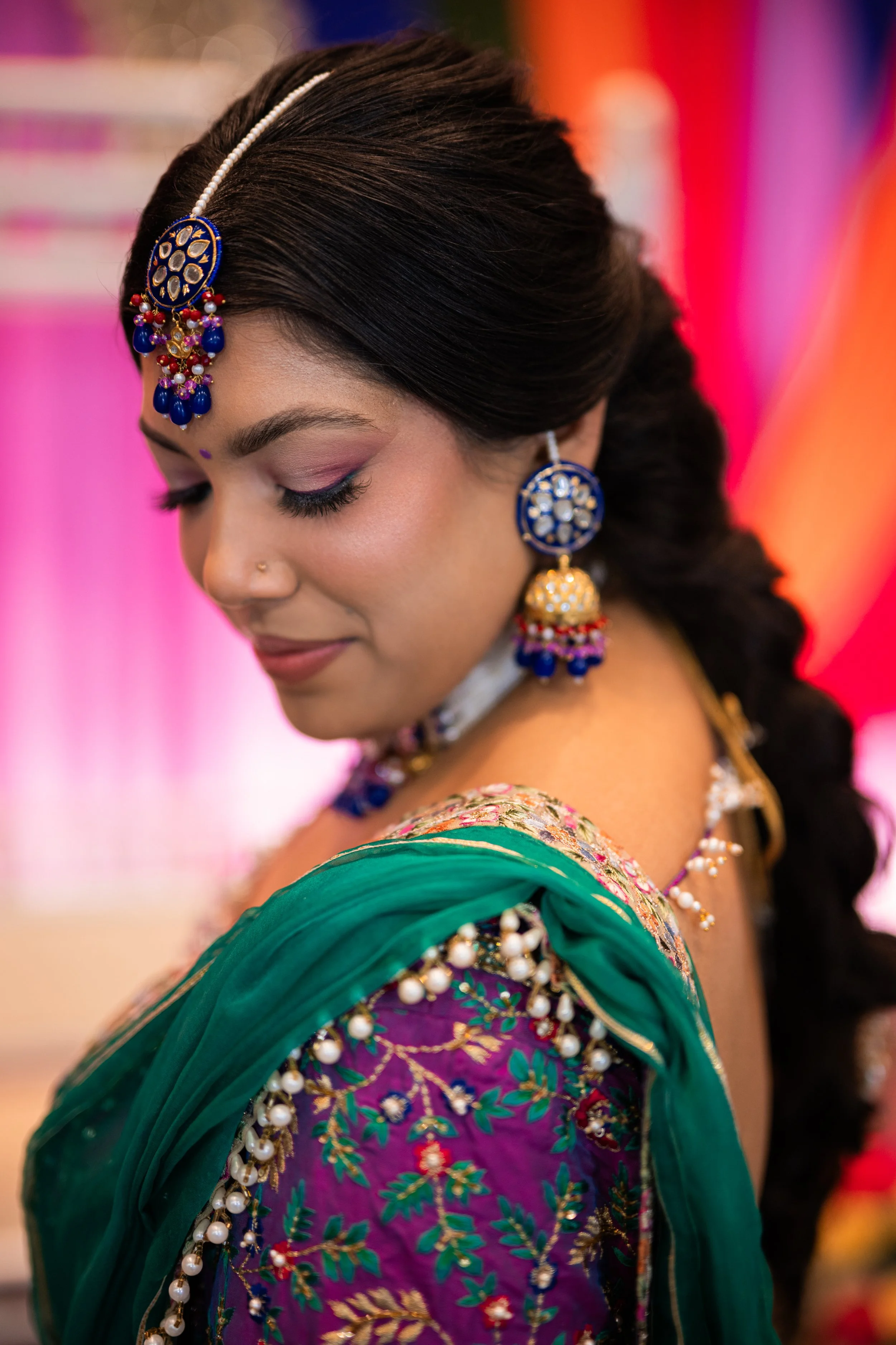 A woman dressed in traditional Indian attire, wearing colorful and ornate jewelry, including earrings and a forehead ornament, with her eyes closed and a serene expression.