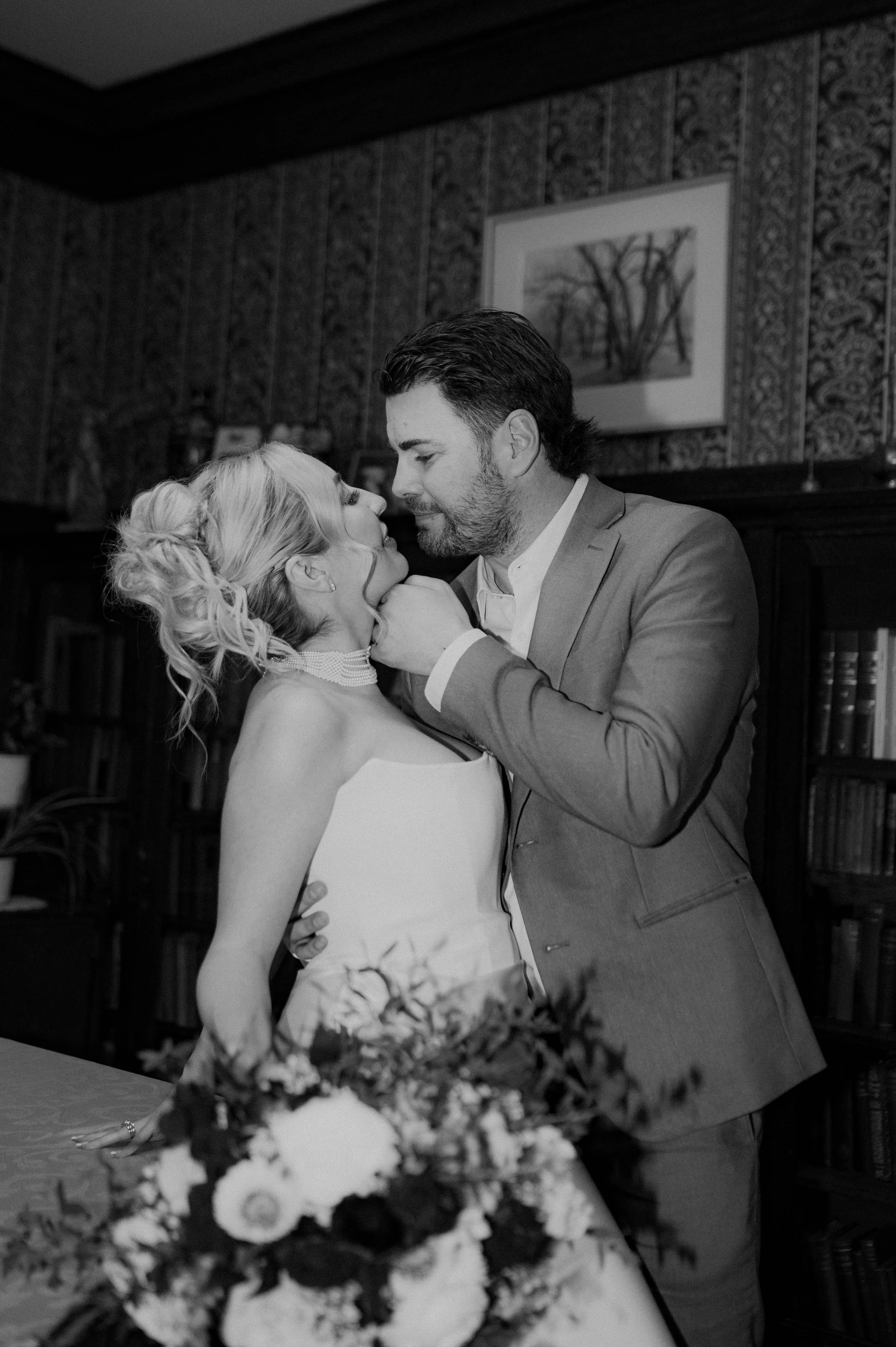 A bride and groom sharing an intimate moment during their wedding dance, with the bride wearing a strapless wedding gown and the groom in a suit, in a decorated indoor setting.