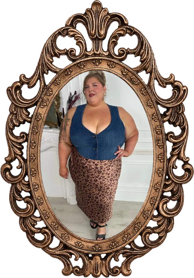 A woman taking a mirror selfie indoors wearing a denim top and a leopard print skirt, with a tattoo on her arm and black heels.