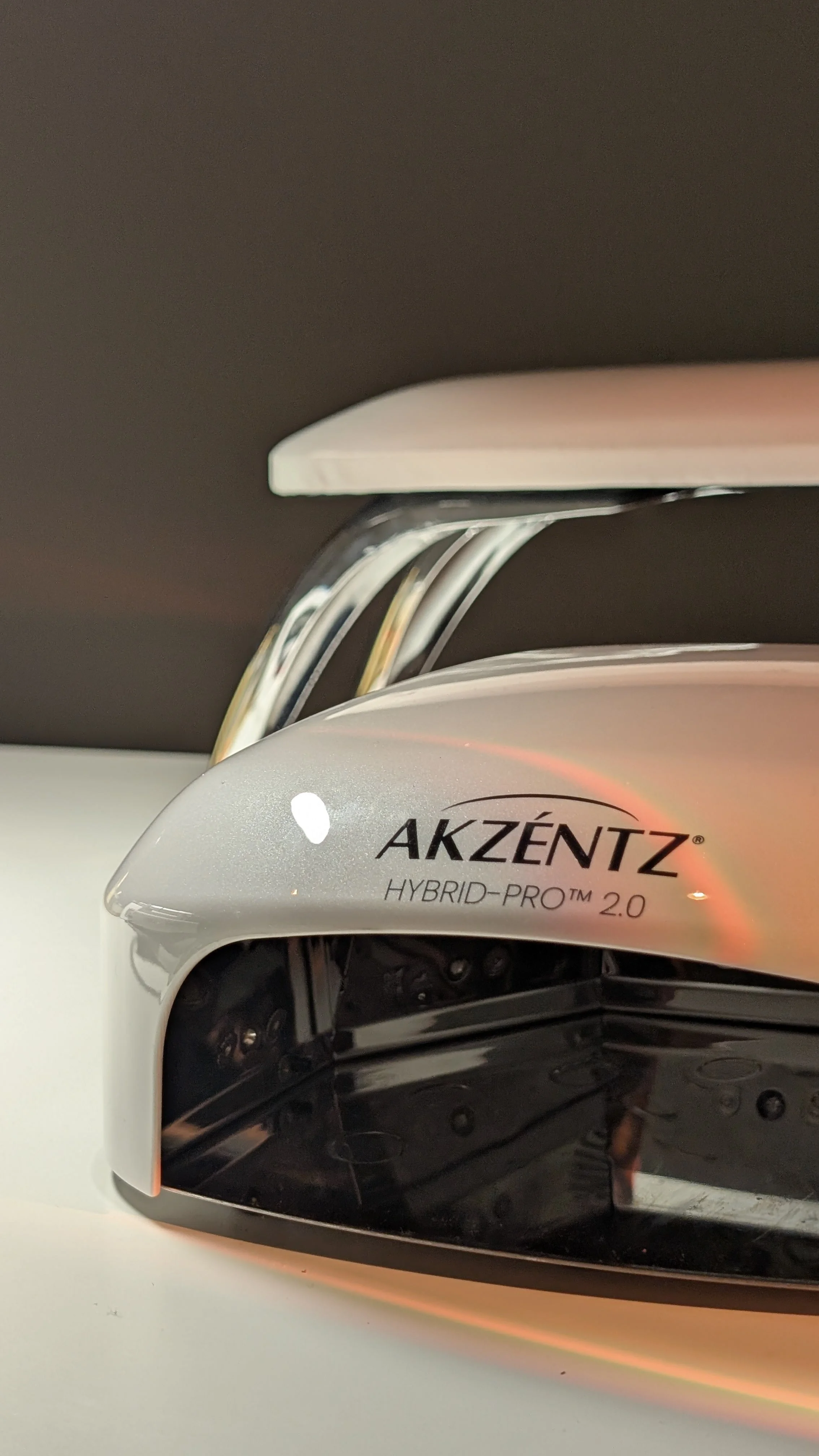 Close-up of an Akzentz Hybrid-Pro 2.0 gel nail lamp with visible interior components, reflecting light on a white surface.