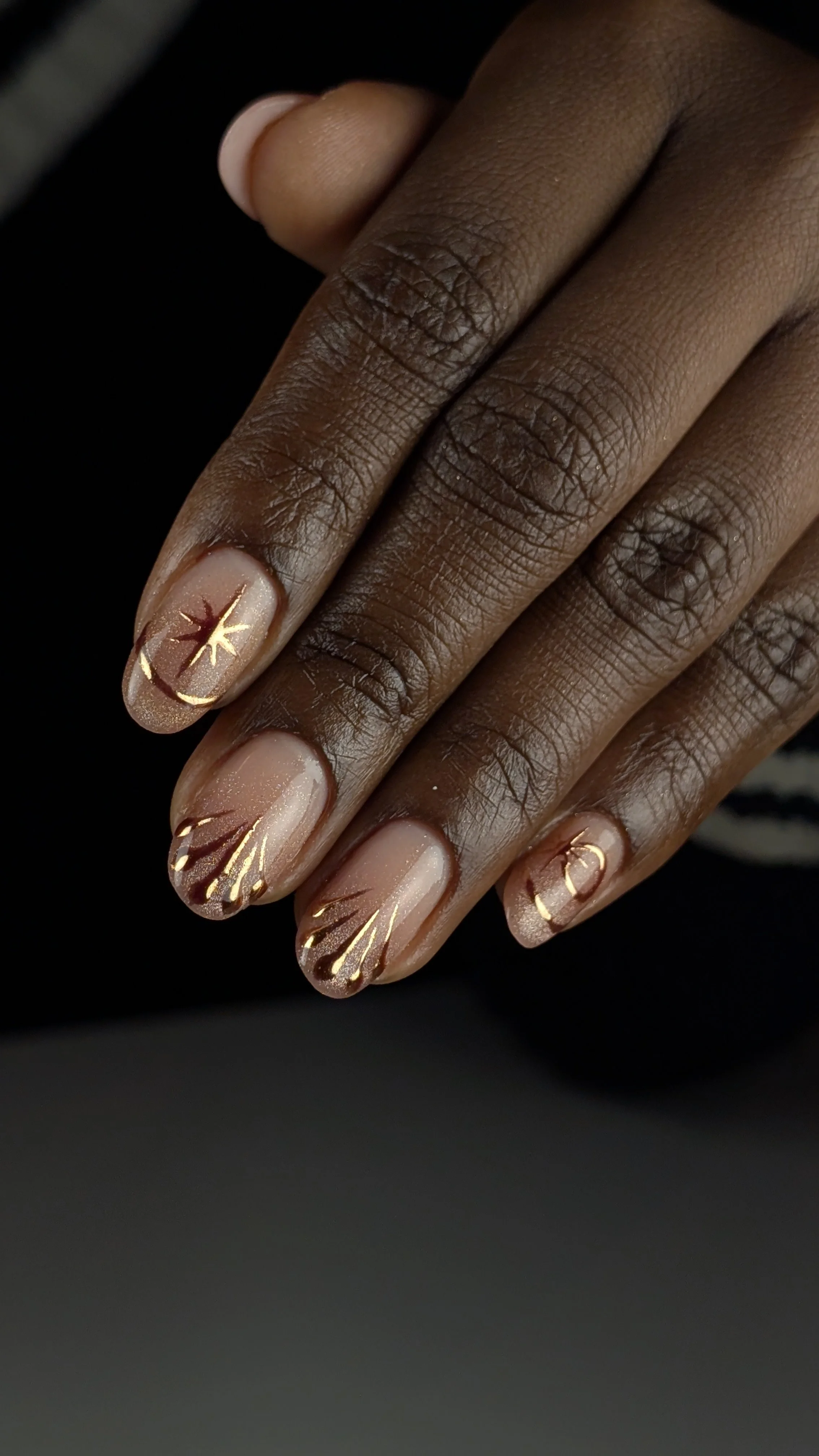 Close-up of a hand with gold and maroon nail art on natural nails.