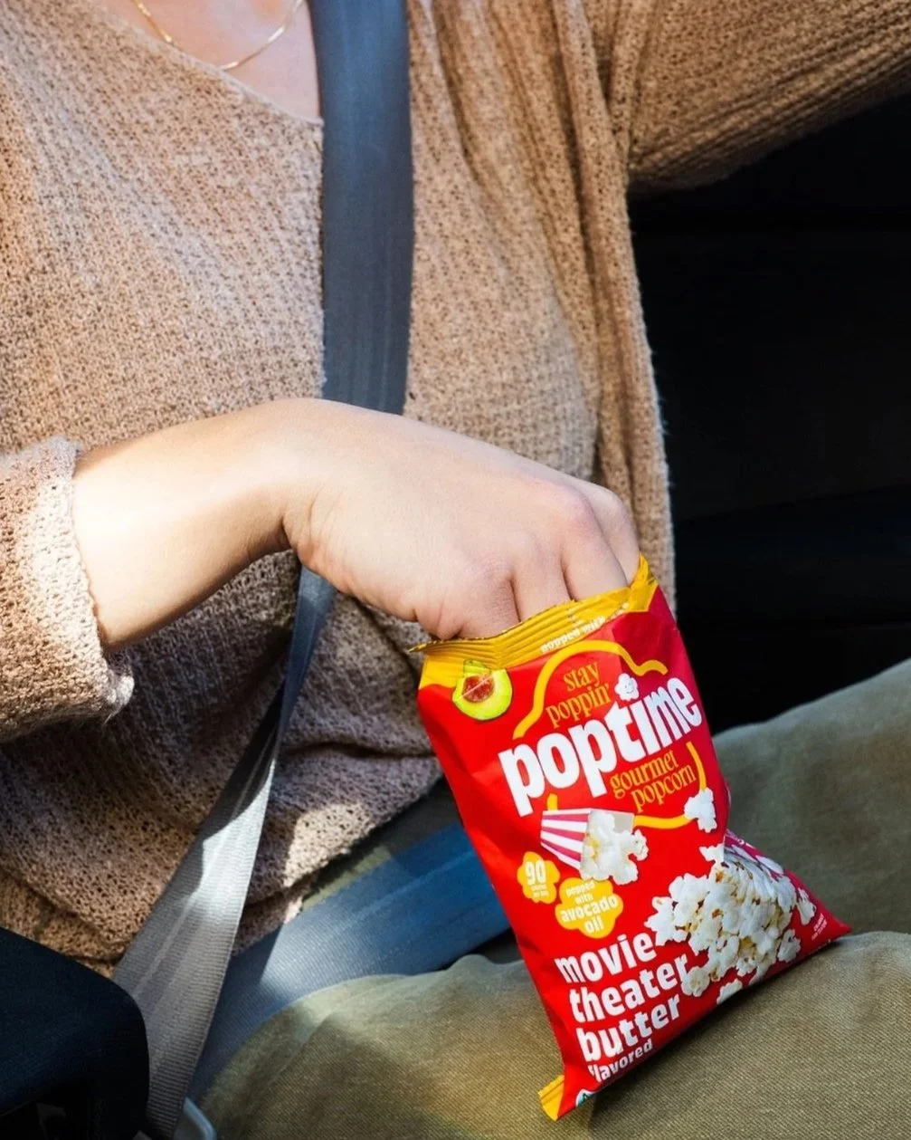 Person holding a bag of Stay Poppin gourmet popcorn with movie theater butter flavor on a bus or car seat.