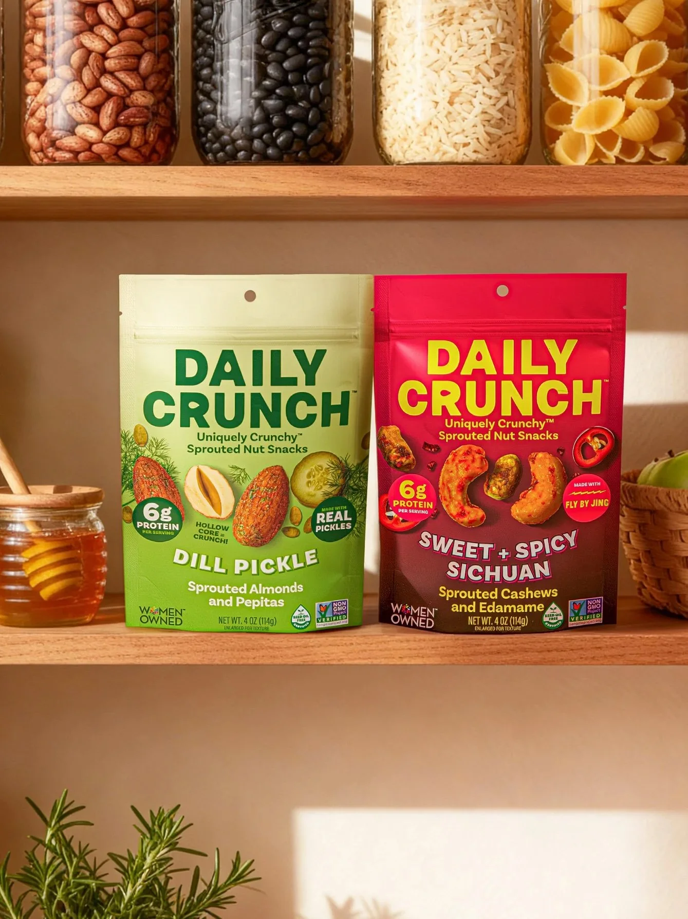 Shelf with glass jars containing beans, rice, and pasta, with two bags of snack foods labeled 'Daily Crunch' in front.