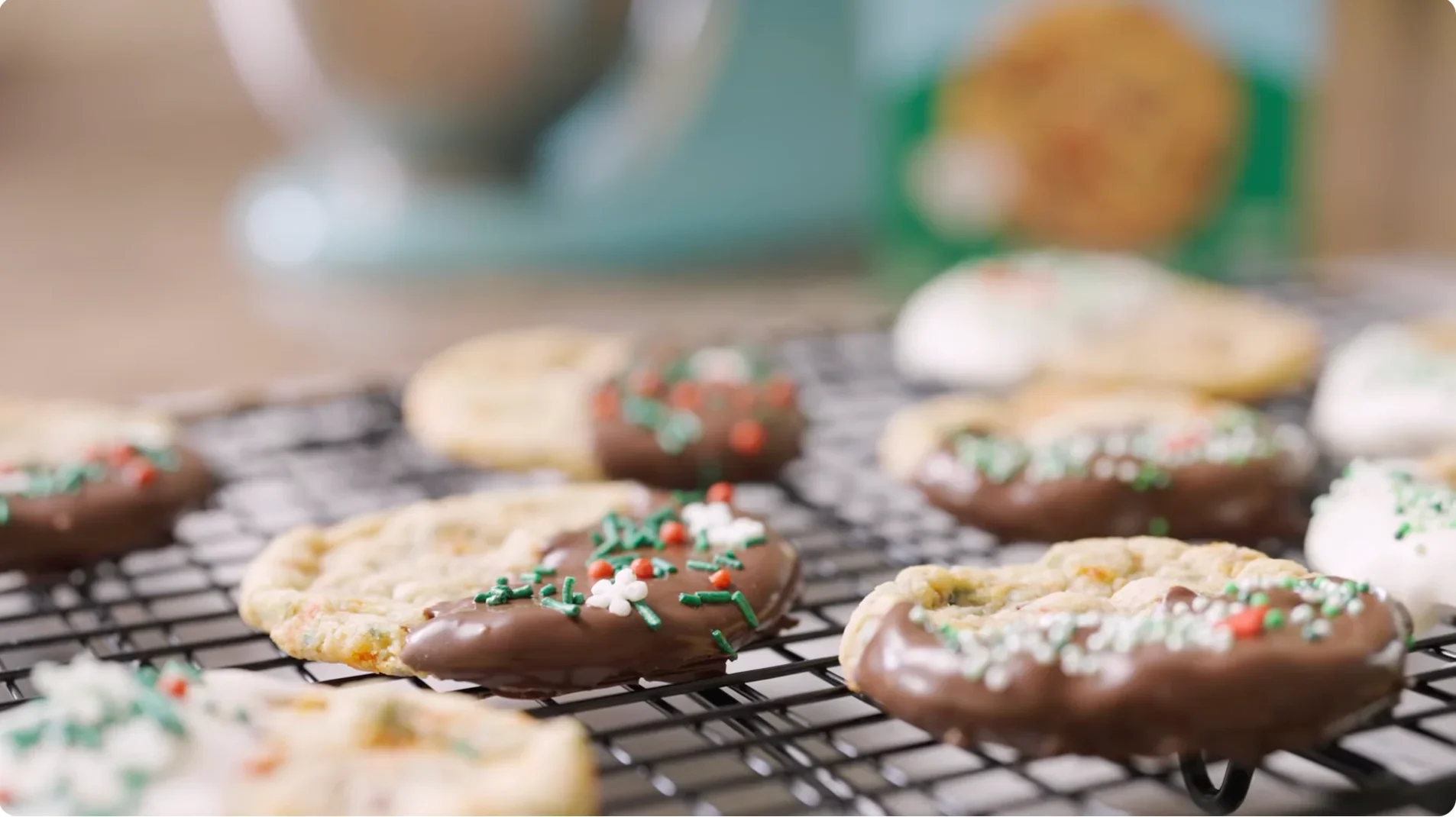 Assorted Christmas cookies decorated with chocolate, sprinkles, and white icing, cooling on a wire rack.