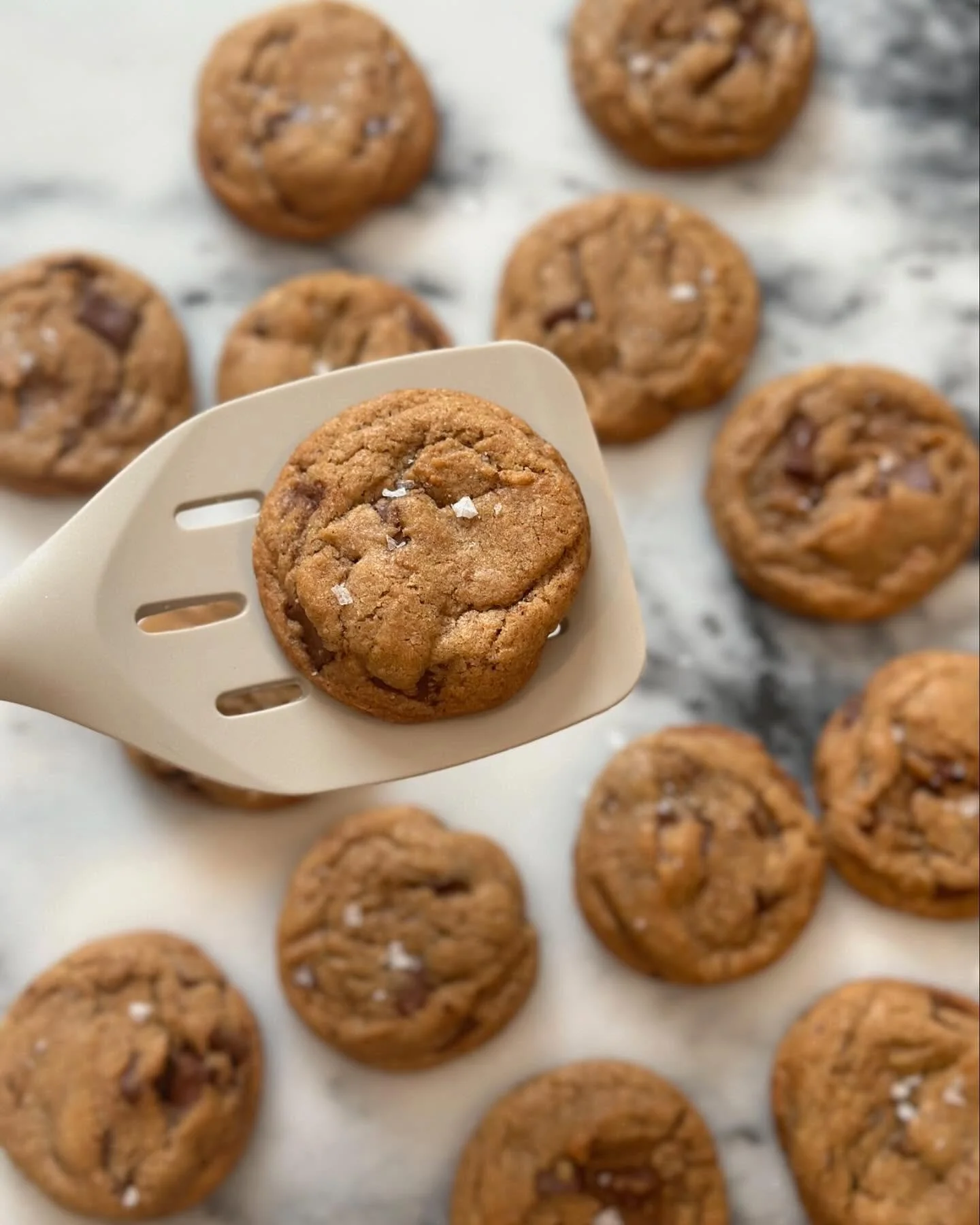 Chocolate chip cookies on a baking sheet, with one cookie being held up on a spatula.