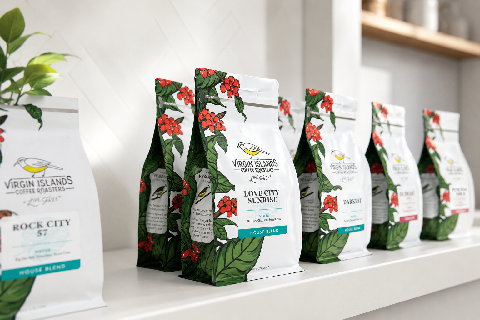 Packages of Virgin Islands Coffee Roasters on a white shelf, featuring colorful botanical designs with red berries and green leaves, including labels for different coffee blends like Love City Sunrise and Darkest.