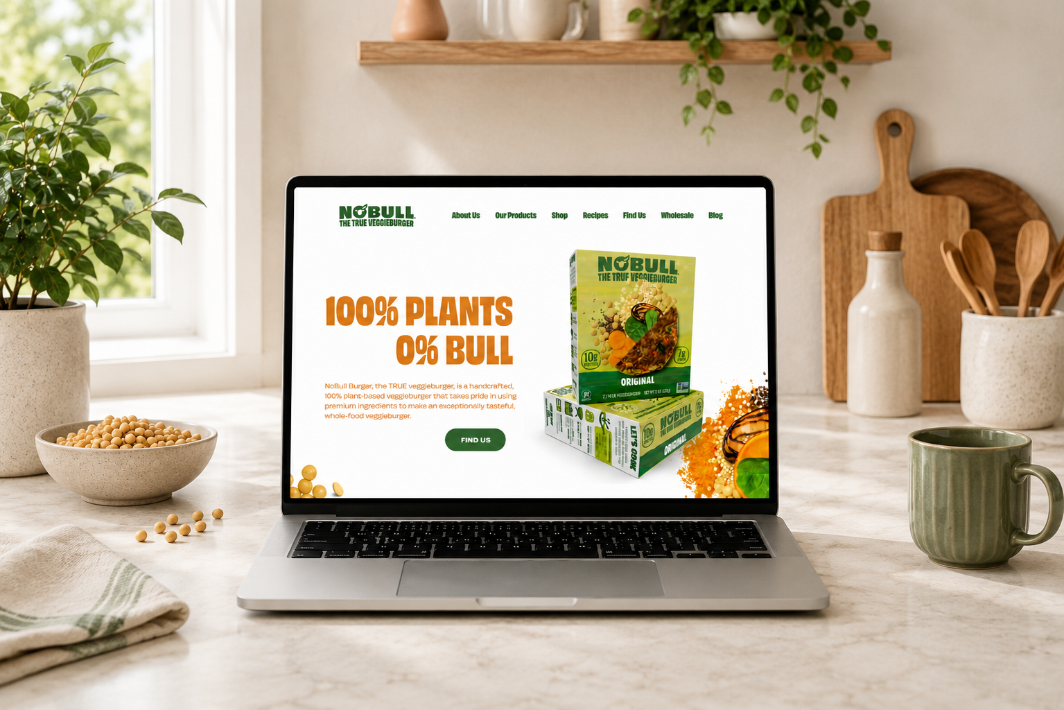 Laptop on kitchen counter displaying a website for NoBull vegan veggie burger with the slogan "100% Plants 0% Bull" and an image of the product packaging.
