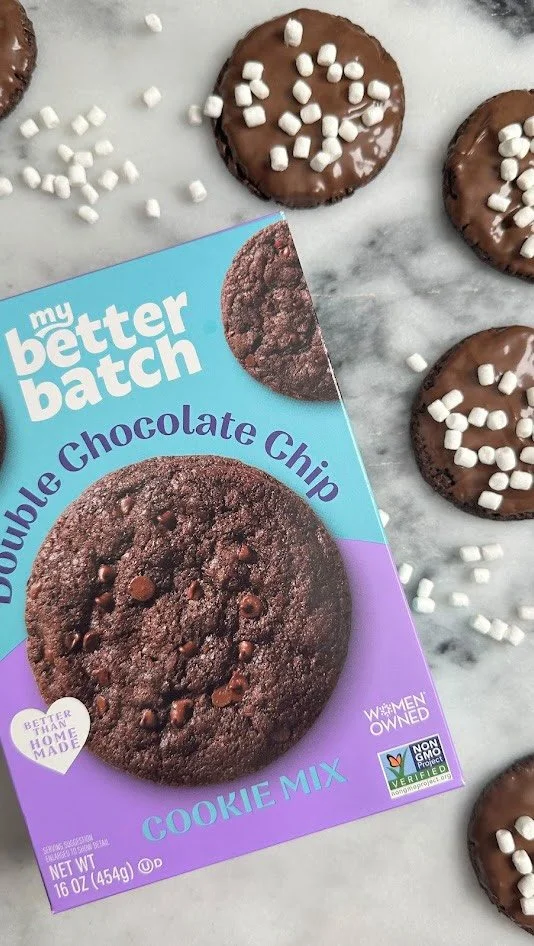 A package of my better batch double chocolate chip cookie mix with cookies topped with chocolate and white sprinkles laid on a marble surface.