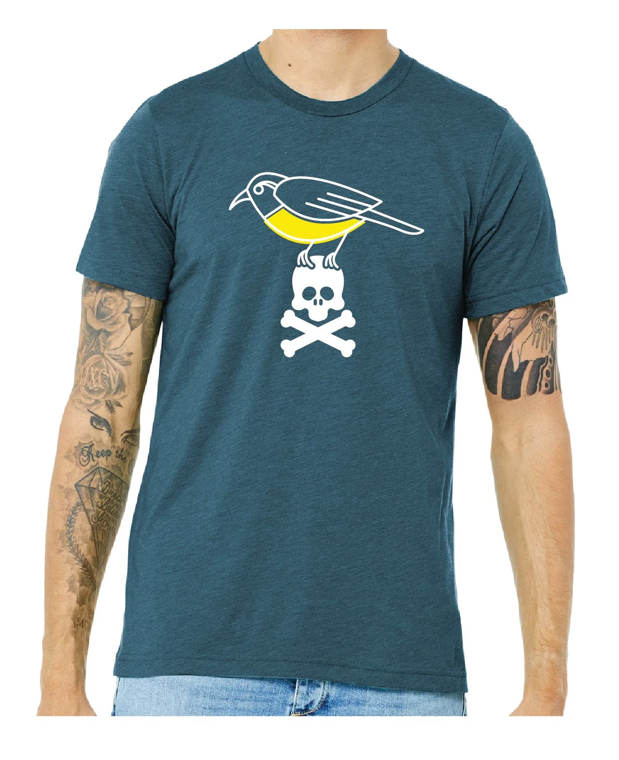 A man wearing a blue T-shirt with a graphic of a bird perched on a skull with crossbones. The man has tattoos on both arms.