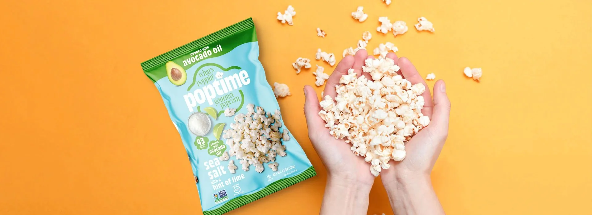 A person holding a handful of popcorn with a bag of popcorn placed nearby on an orange and yellow background.