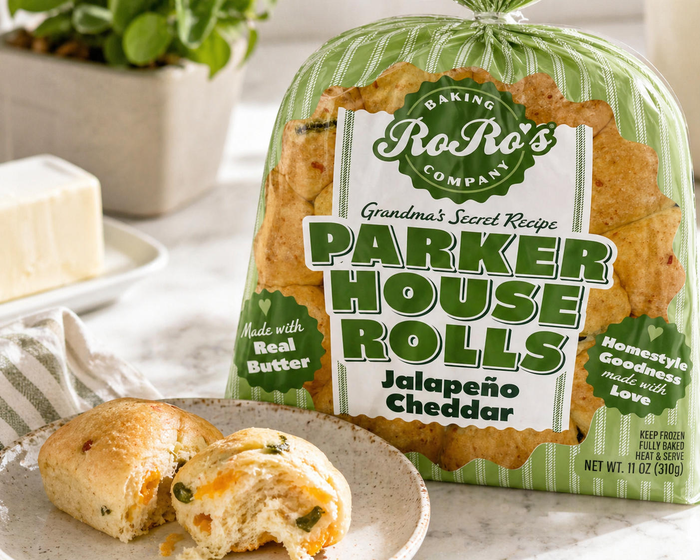 A bag of RoRo's Bakery Parker House Rolls with Jalapeno Cheddar flavor, with some rolls on a plate in front. The bag is green and white, featuring labels about real butter and homemade goodness.