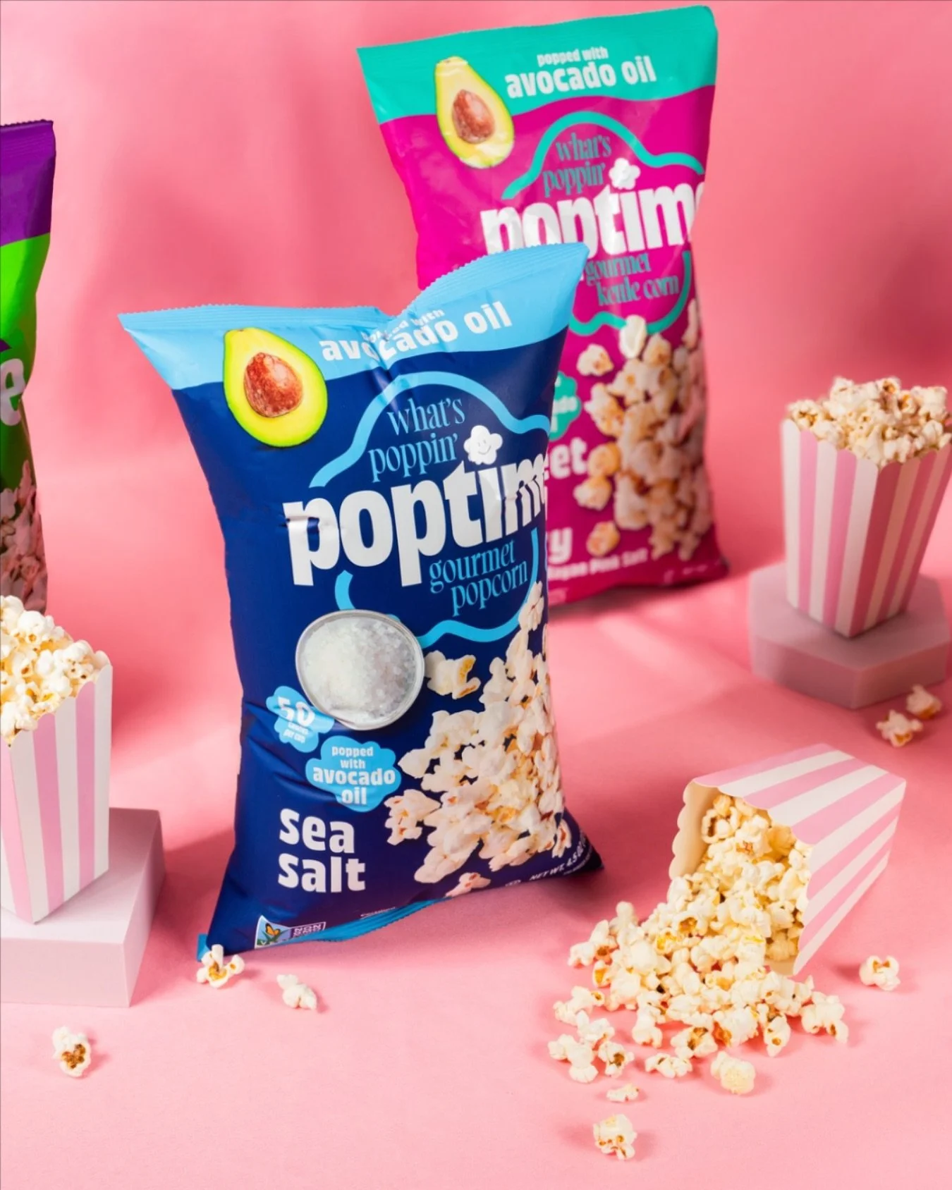 Two bags of popcorn, one blue labeled 'sea salt' and one pink labeled 'butter,' with popcorn spilling out into small striped pink and white containers on a pink background.
