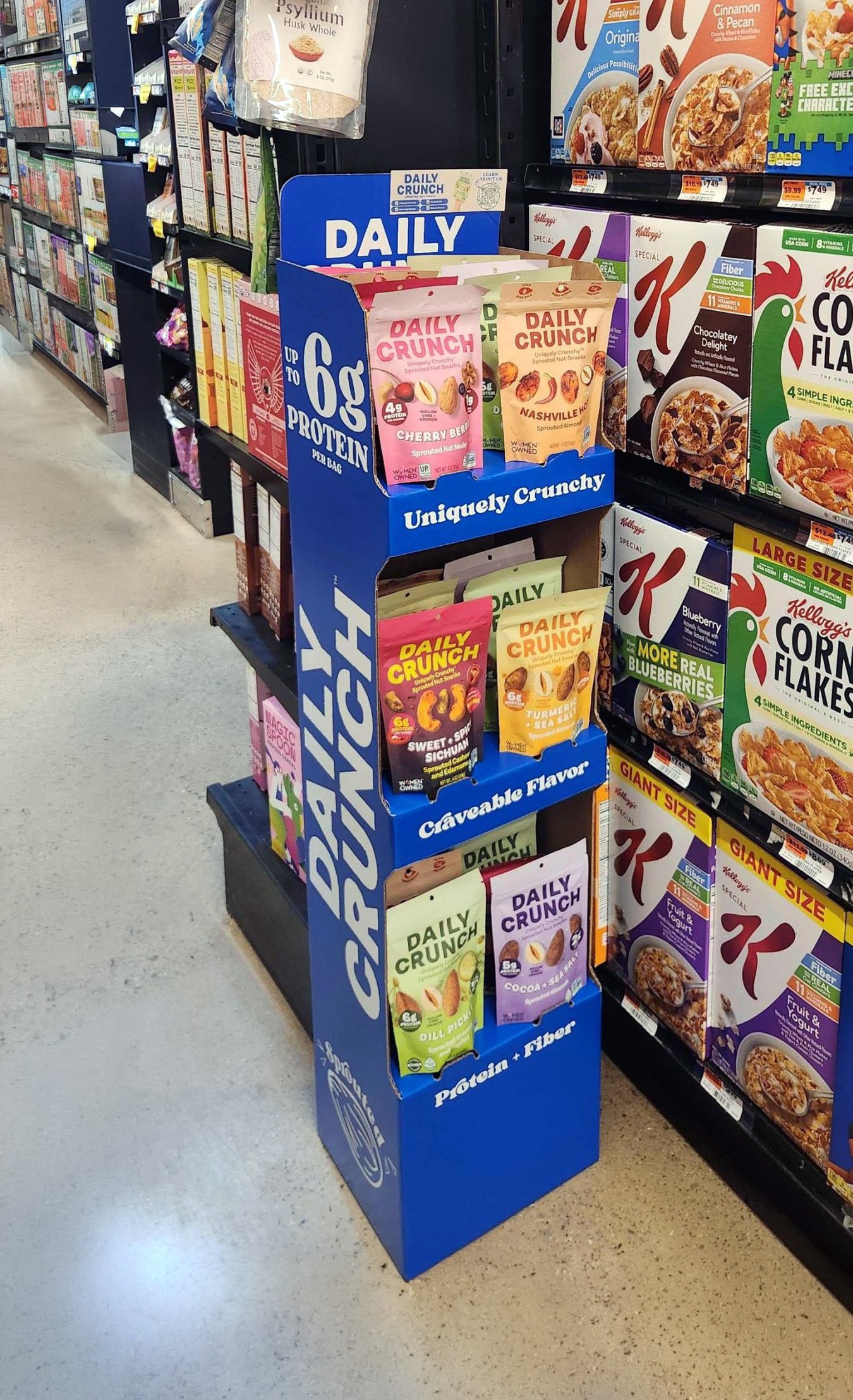 Display stand in a grocery store aisle holding various flavors of Daily Crunch snack packs.
