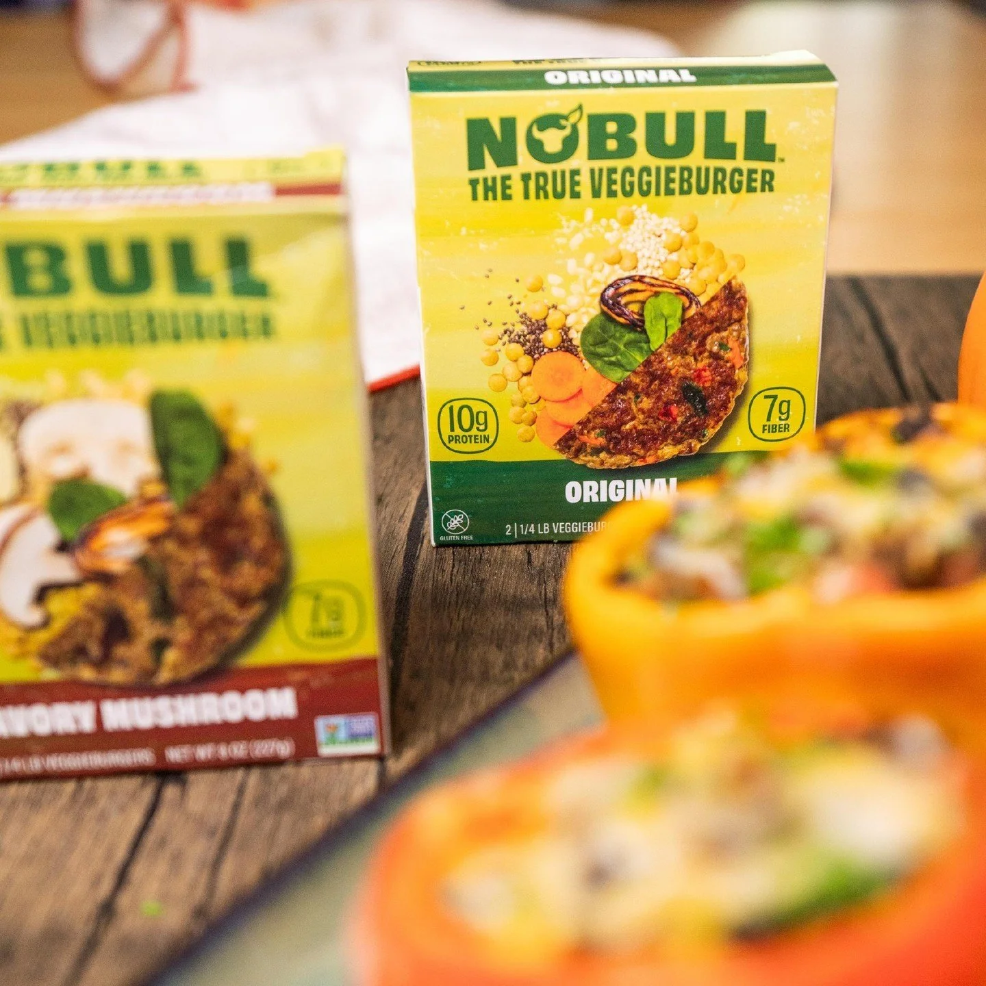 Boxes of Nobull veggie burger patties on a wooden surface, with a colorful veggie burger in the foreground.
