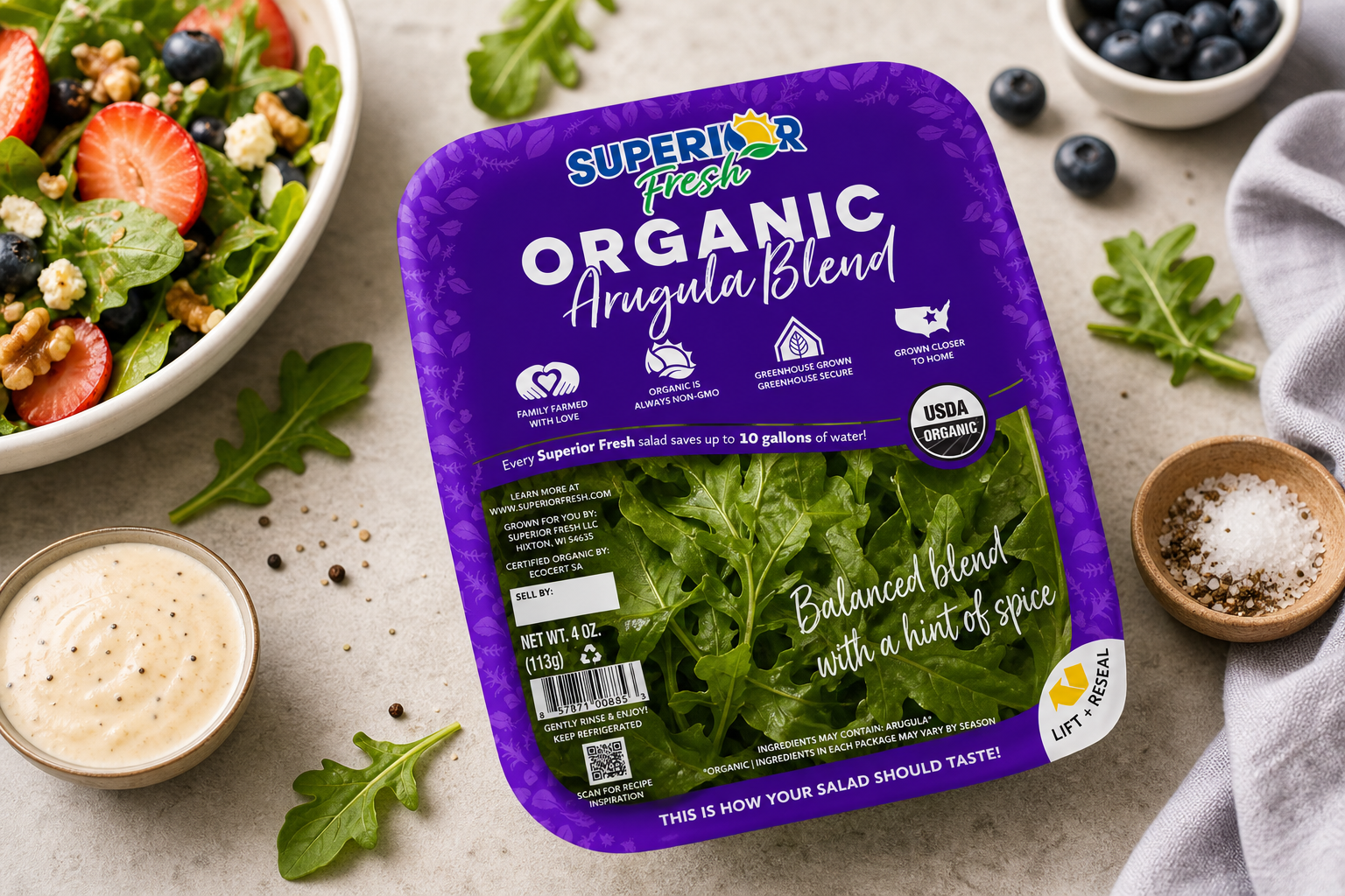 Package of Superior Fresh organic arugula blend with fresh arugula leaves visible through the clear window. The packaging is purple with white text and symbols indicating it is family farmed, non-GMO, greenhouse grown, and grown closer to home.