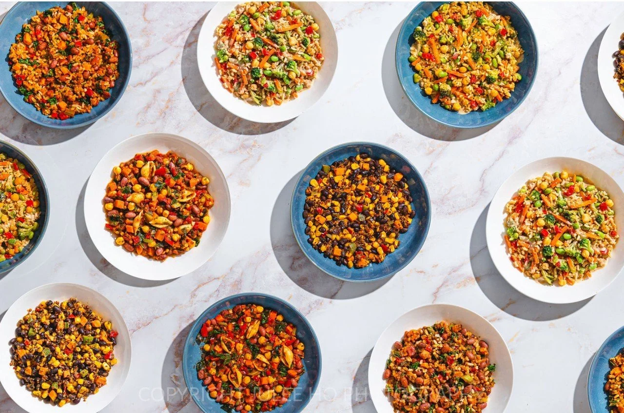 Colorful bowls of cooked mixed vegetables arranged on a white marble surface.