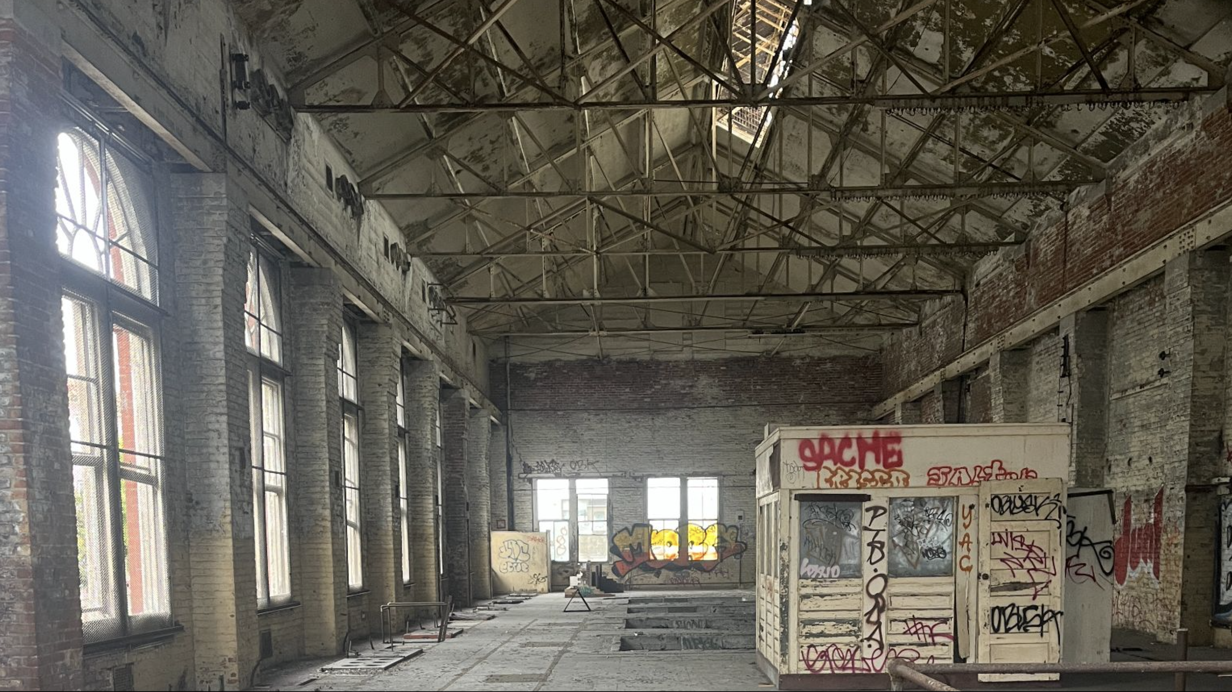 Interior of the Fillmore Substation building with large arched windows, graffiti-covered storage units, and a damaged ceiling with metal beams.