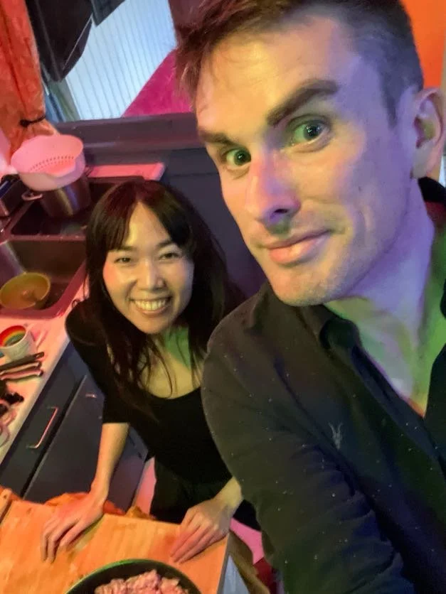 Cadence for Change members smiling in a kitchen, with the man taking a selfie. The kitchen has a countertop with bowls and utensils, and a pink kettle in the background.
