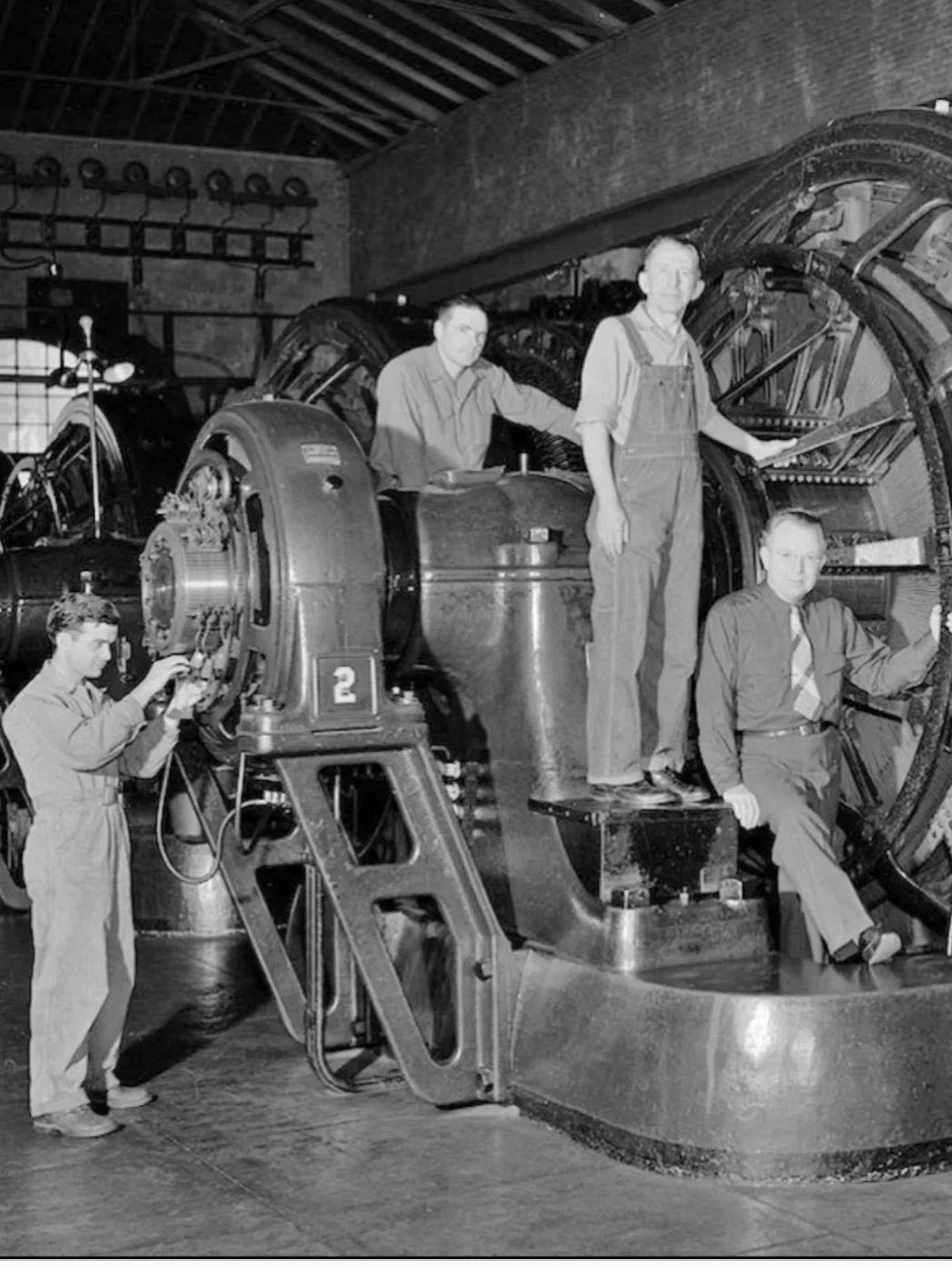 Black and white photo of four men working on a large mechanical device, possibly an engine or machinery in an industrial setting.