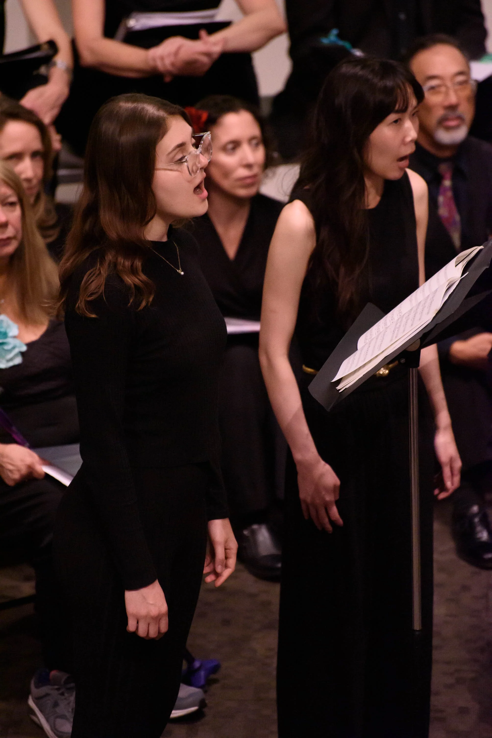 Cadence for Change members standing in a choir, singing, with music sheets on a music stand in front of them.