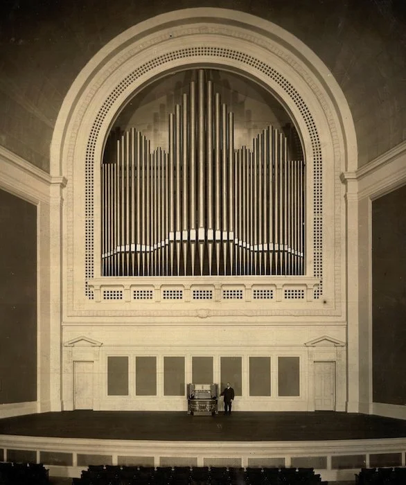 Large concert hall stage with a massive pipe organ, the San Francisco Exposition Organ, and a person standing next to a smaller organ or console.