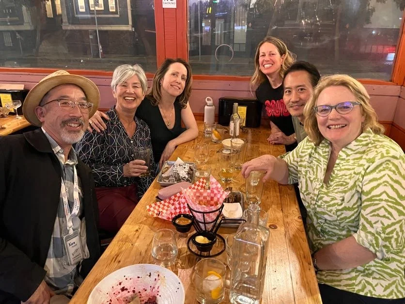 Cadence for Change members sitting around a wooden table in a restaurant, smiling and enjoying drinks.
