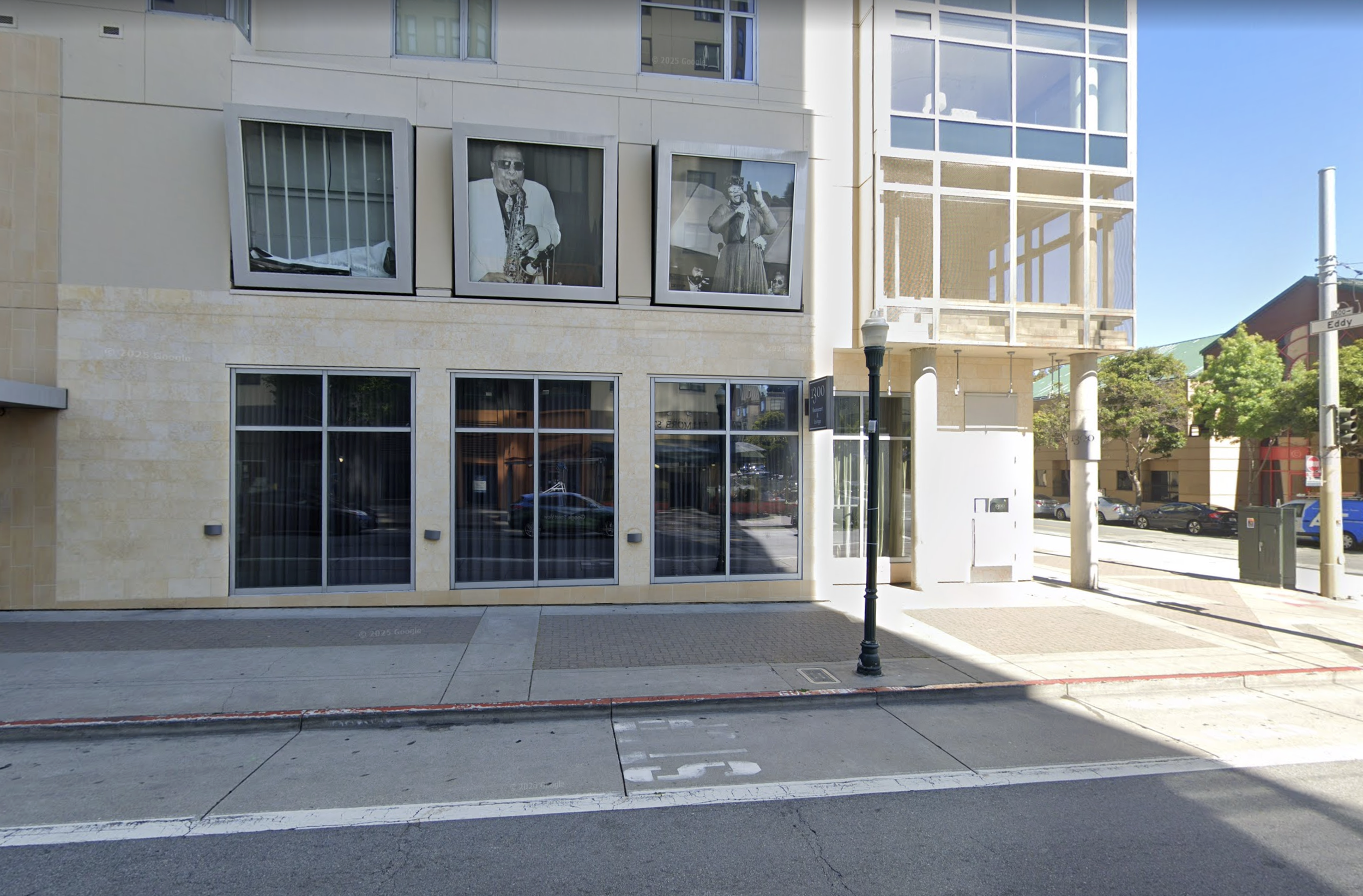Street view of a modern building, the Fillmore Heritage Center, with large windows, including framed black-and-white photographs of people; a sidewalk and street are visible in the foreground, with a lamppost and trees on the corner.