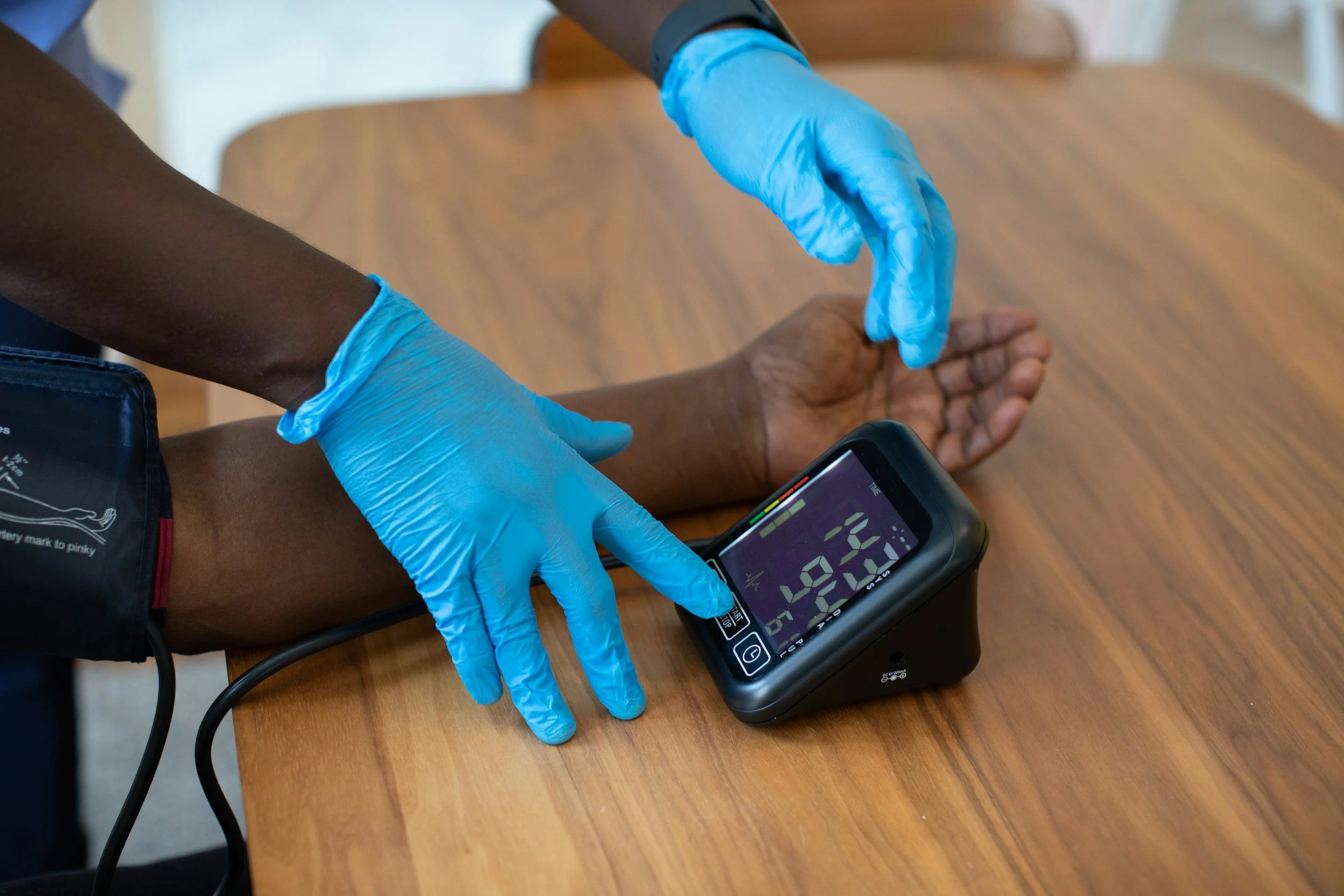 A medical professional wearing blue gloves measuring a patient's blood glucose level with a digital glucose monitor on a wooden table. Hospice, home health, revenue, QAPI