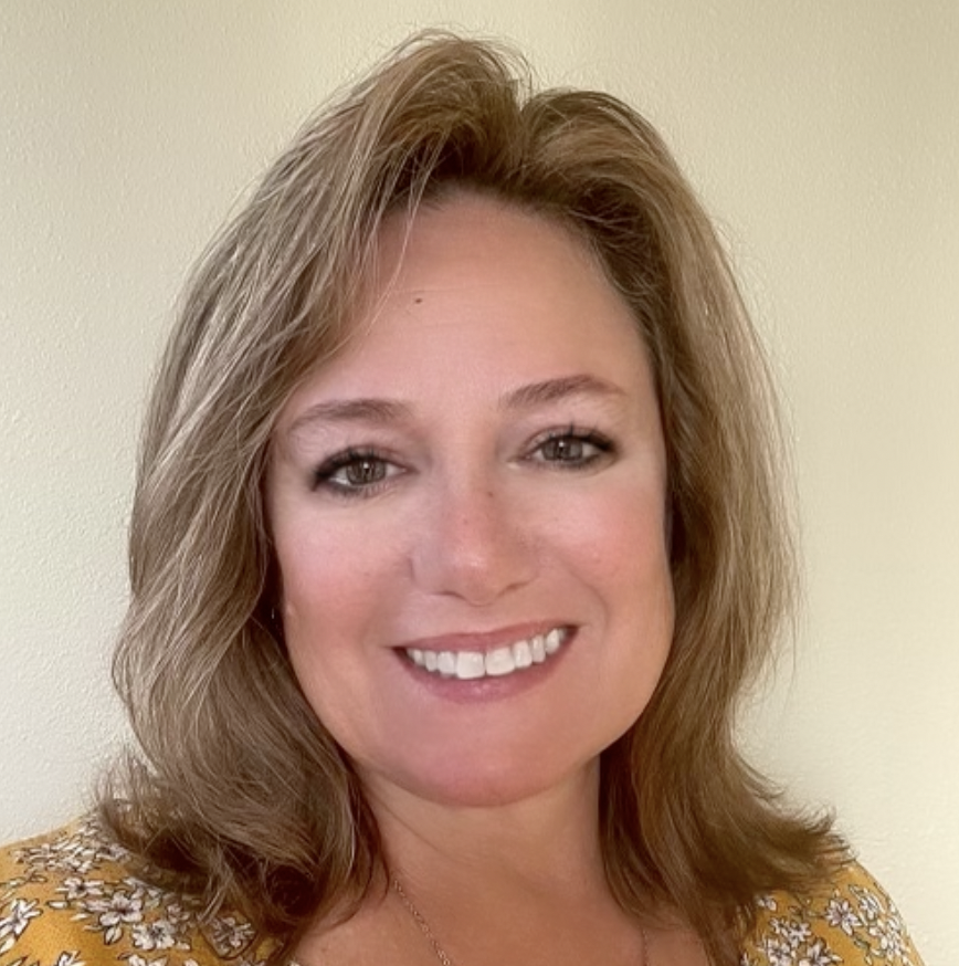 A woman with shoulder-length light brown hair, smiling, wearing a yellow floral top, standing against a plain light-colored wall. Pam Arnold, Hospice, home health, revenue, QAPI