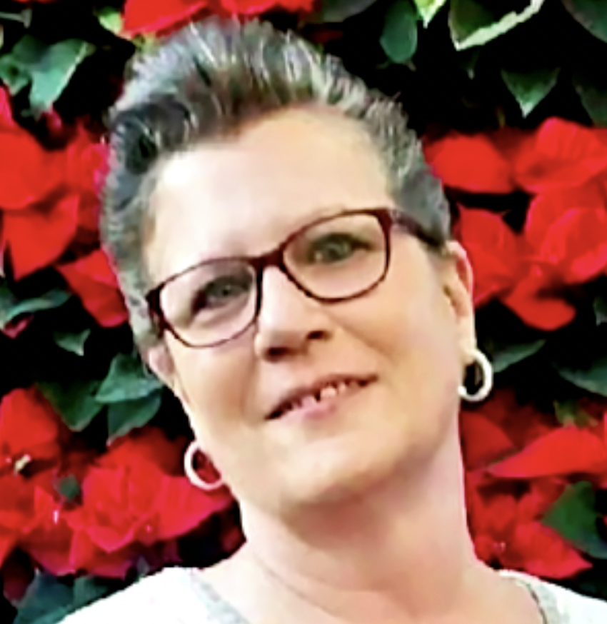 A woman with short gray hair, glasses, and hoop earrings smiling in front of red poinsettia flowers. Jennifer Mayle, HR, Hospice, home health, revenue, QAPI