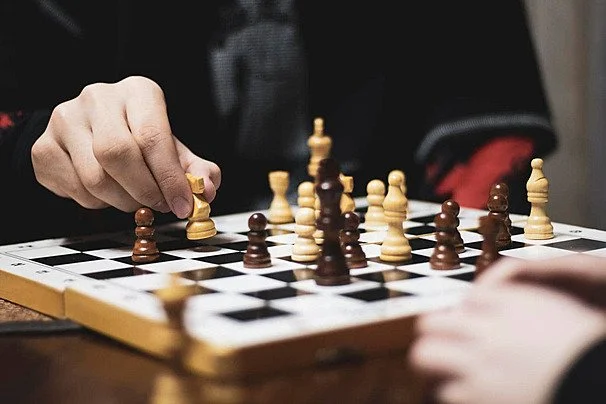 A person making a move in a game of chess on a board with black and white squares, with chess pieces, including pawns and a king, arranged on the board.