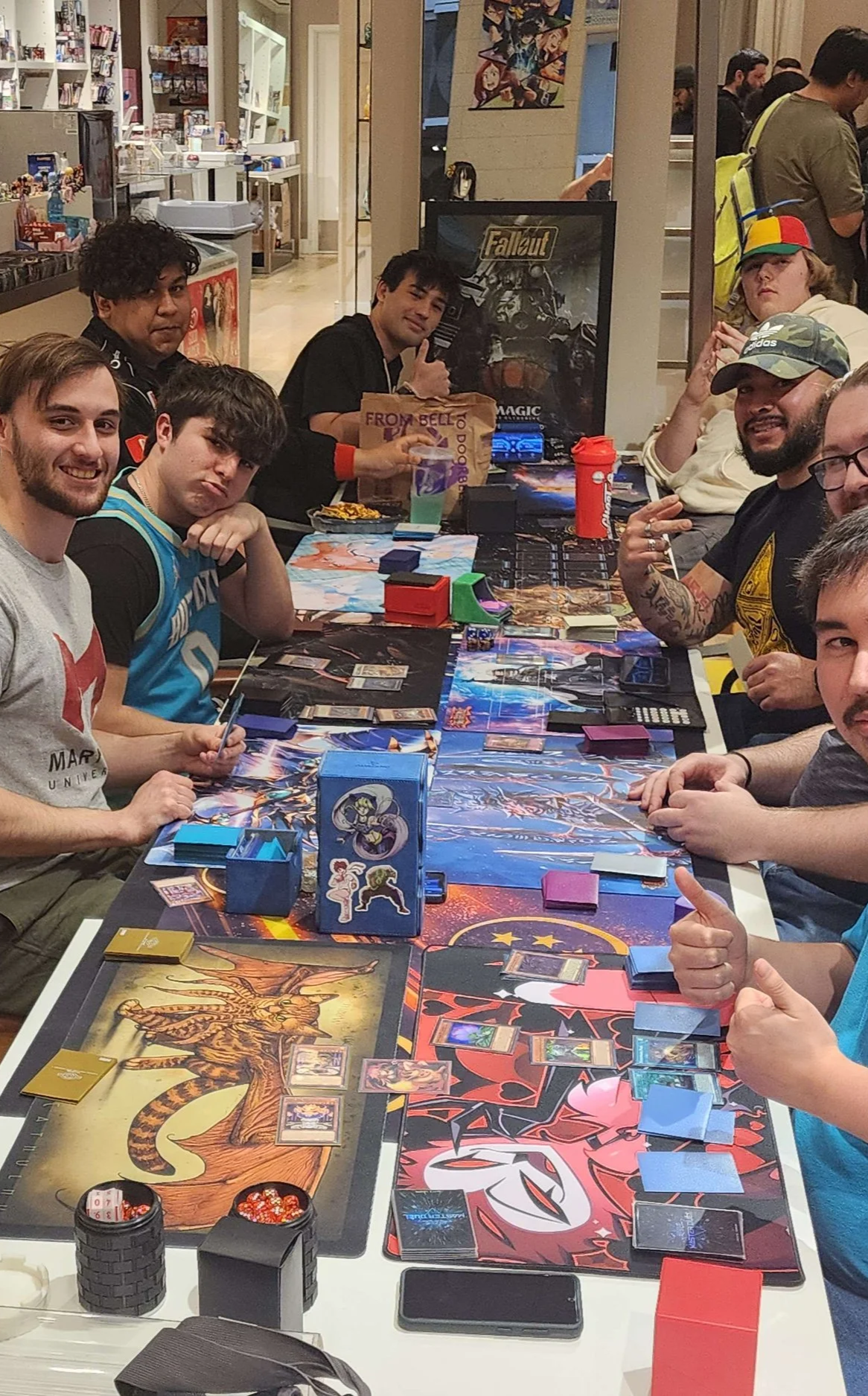 Group of people playing card and board games at a gaming tournament or event in a shopping mall.