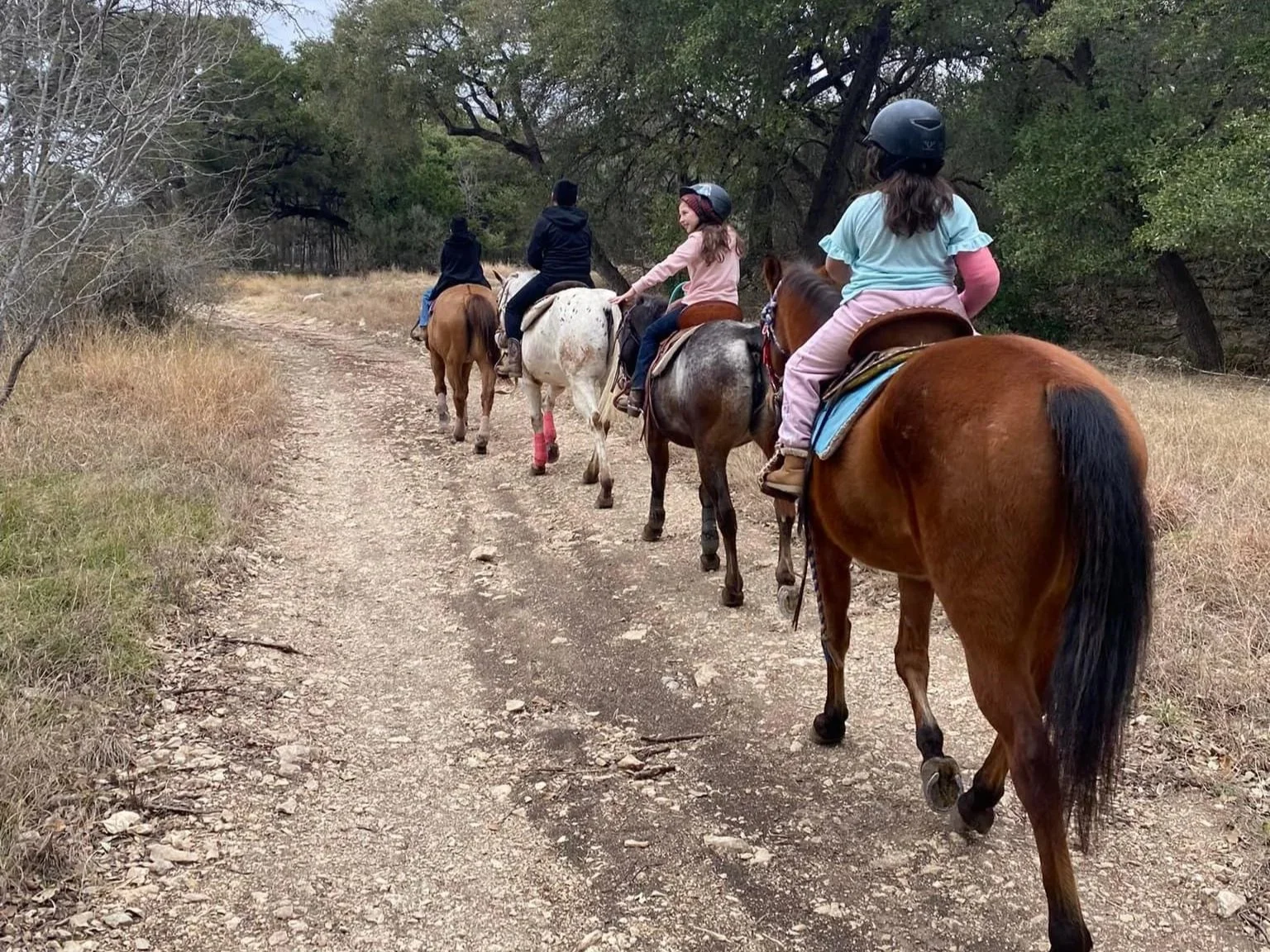 Family group riding single file on a trail at The Gentle Cowgirl in Stockdale, TX — guided trail rides for kids and adults near San Antonio