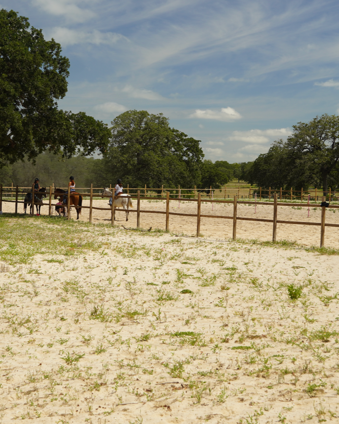 Riders in the outdoor sand arena at The Gentle Cowgirl in Stockdale, TX — spacious western riding arena available for boarding horses and riding lessons near San Antonio