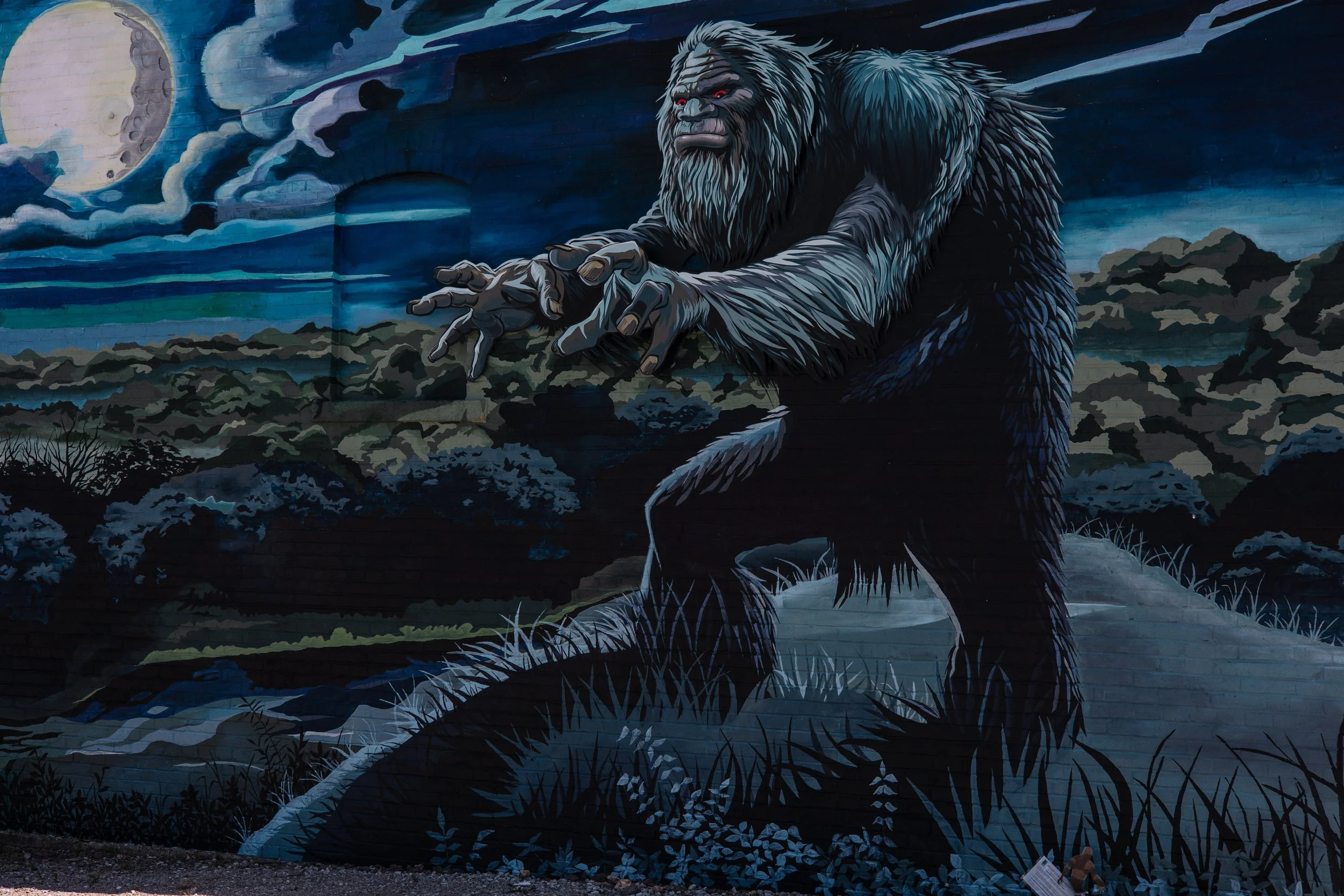 painted mural on brick wall of big muddy monster creature standing with forest river