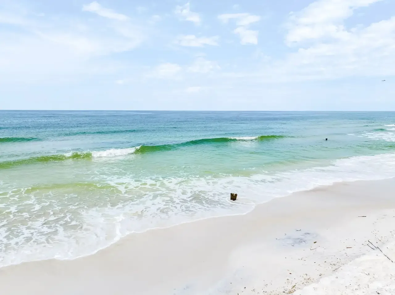 A peaceful beach scene with gentle waves, white sand, and a partly cloudy sky.