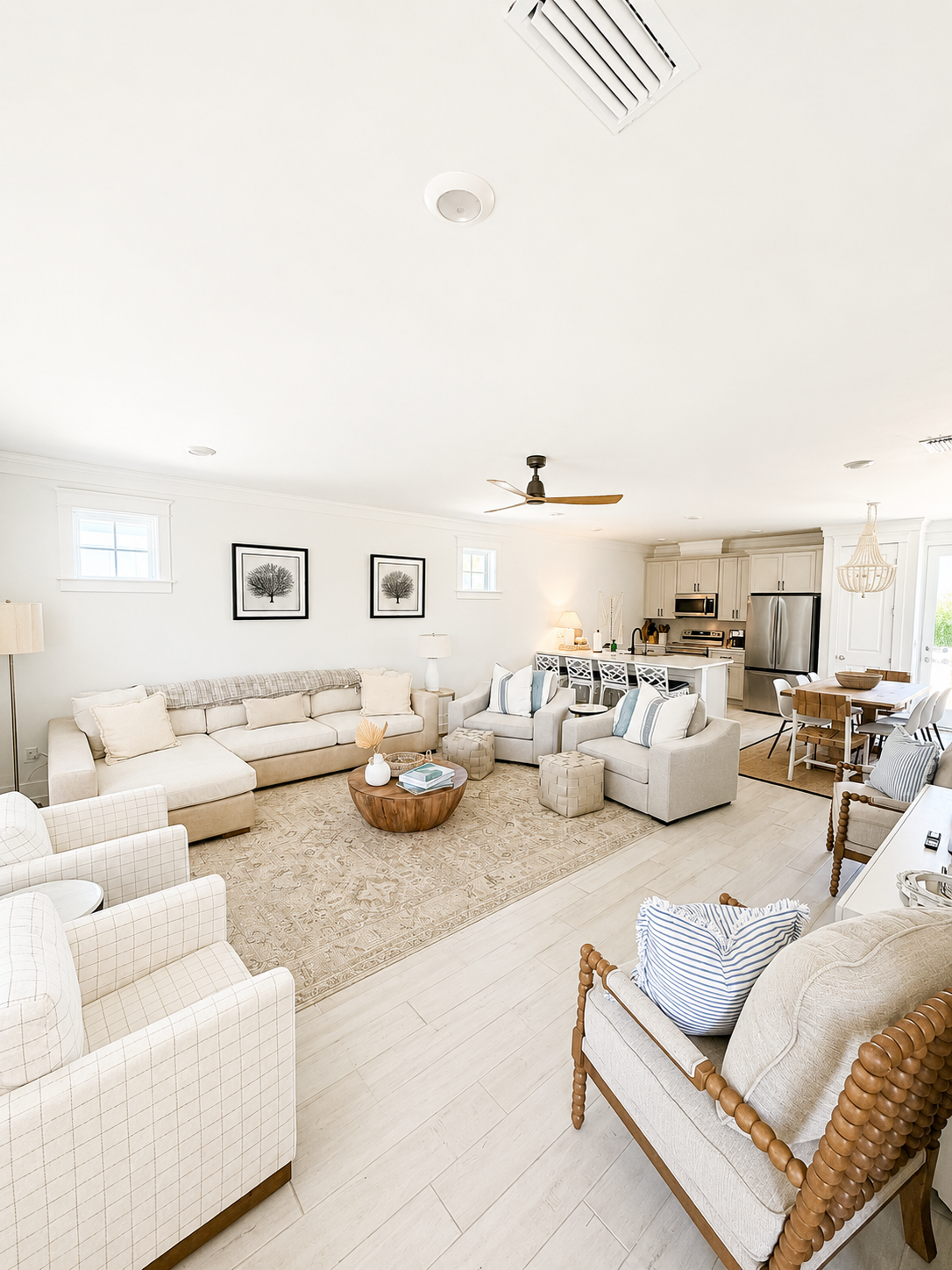 Bright, open living room with white walls, beige furniture, a wooden coffee table, and kitchen in background.