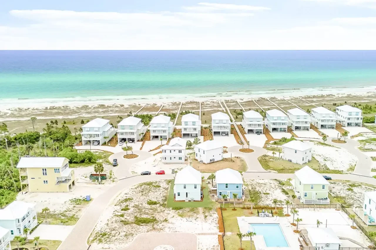 Aerial view of a beachfront neighborhood with houses facing the ocean, sandy beach, and ocean water with shades of blue and green.