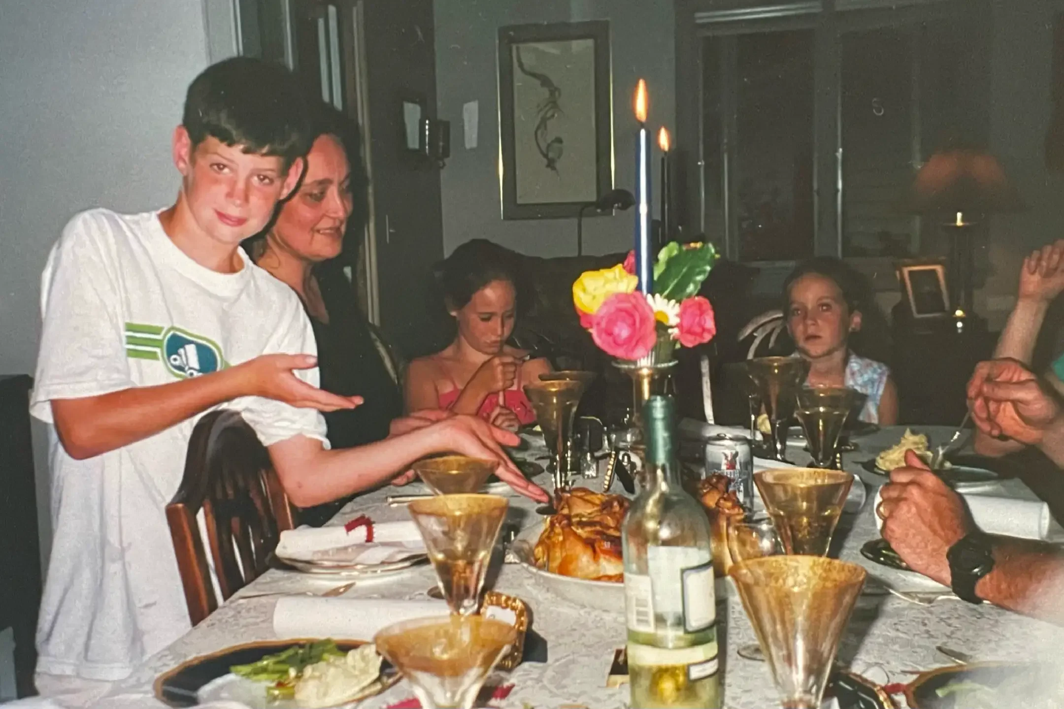 A family gathering at a dinner table with food, candles, and drinks. A woman is celebrating a birthday with cake and candles.