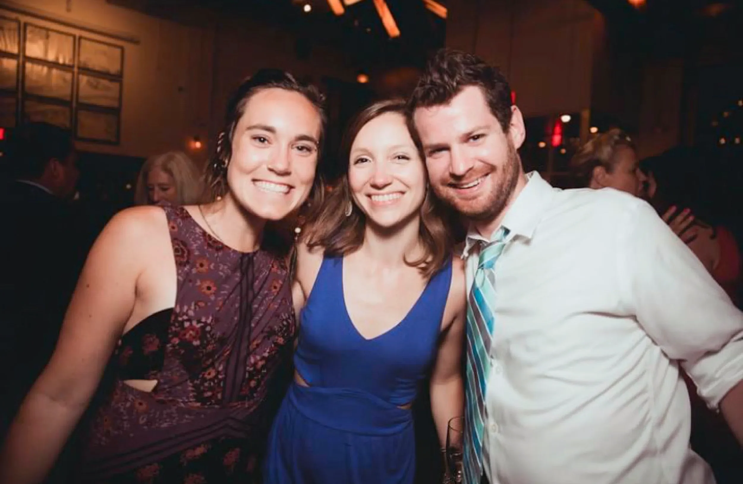 Three friends smiling at a social gathering or party, close together and looking happy.