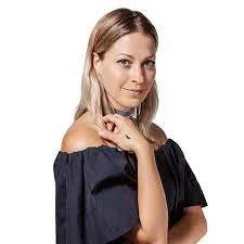 A woman with blonde hair wearing an off-the-shoulder navy blue top, looking at the camera with a slight smile.