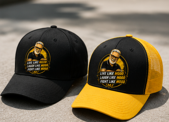 Two baseball caps, one black with a black brim, the other black and yellow with a yellow brim, both featuring a cartoon image of a man with glasses and gray hair, and text that says "Live like MOOD, Laugh like MOOD, Fight like MOOD." the caps are on a concrete surface.