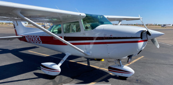 Small private airplane parked on the tarmac at an airport under a clear blue sky.
