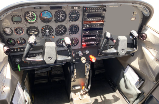 Aircraft cockpit dashboard with multiple analog gauges, switches, and control yokes.