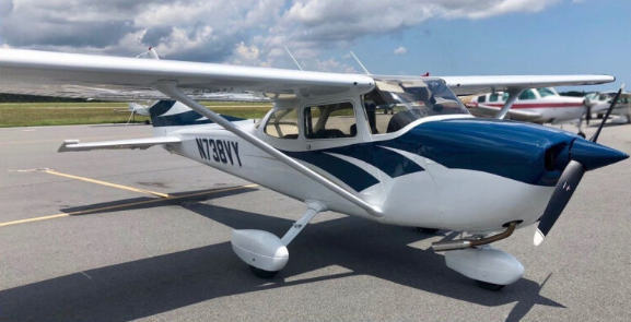Small private propeller airplane parked on the tarmac under a partly cloudy sky.