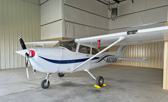 Small white airplane with blue stripe parked inside a hangar.