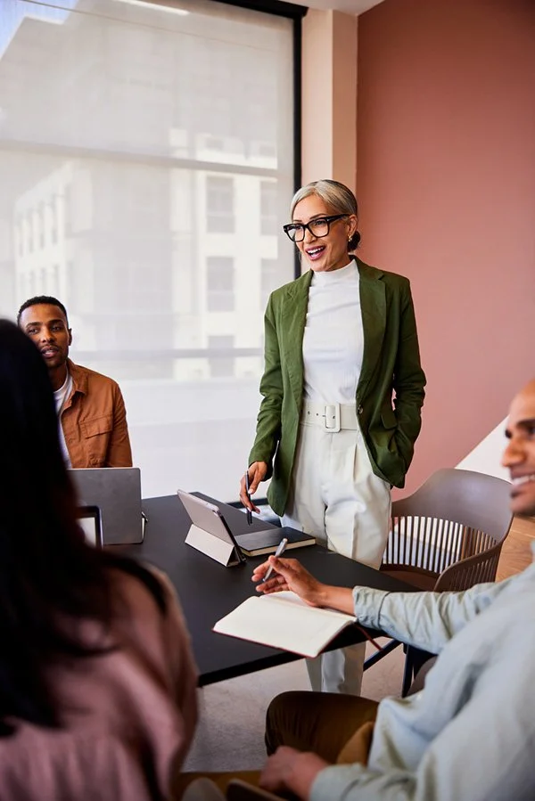 Woman in green blazer and glasses leading team meeting