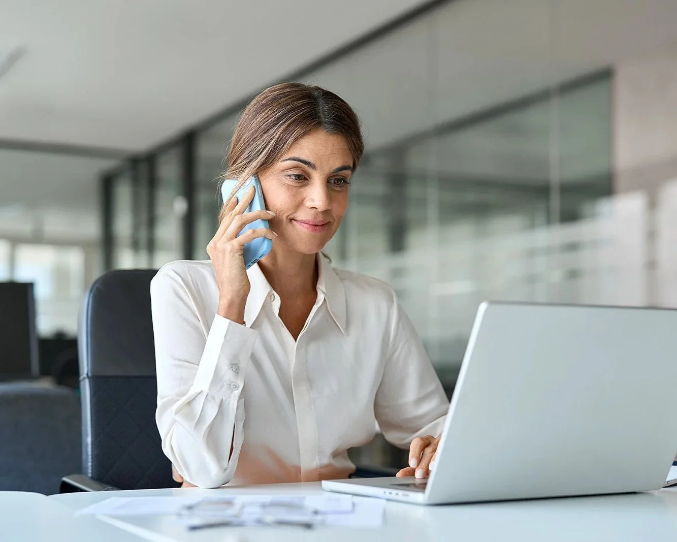 Professional woman smiling while making phone call and looking at her computer