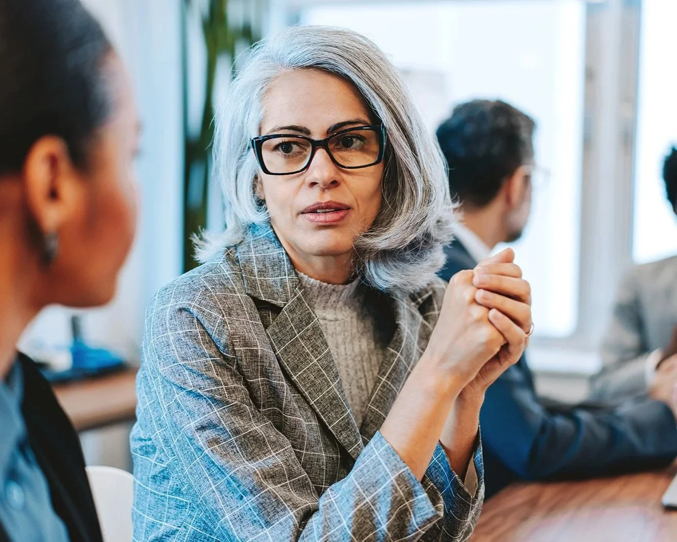 Professional woman in blazer and glasses holding her hands and looking pensive